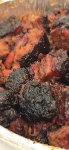 Close-up of smoked brisket burnt ends with a dark, caramelized bark and juicy interior, served in a foil tray.