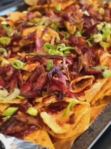 Loaded nachos topped with chopped smoked meat, barbecue sauce, melted cheese, and sliced green onions.