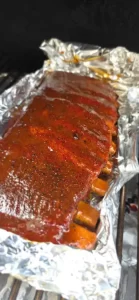 Rack of barbecue pork ribs coated in a glossy sauce, resting on foil inside a grill.